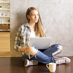 Junge Fraue sitzt mit Laptop und Kaffee am Boden