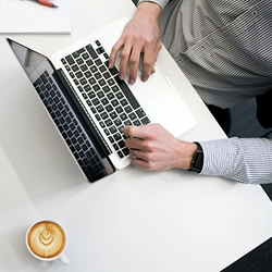 Mann mit Kaffee sitzt an einem Laptop